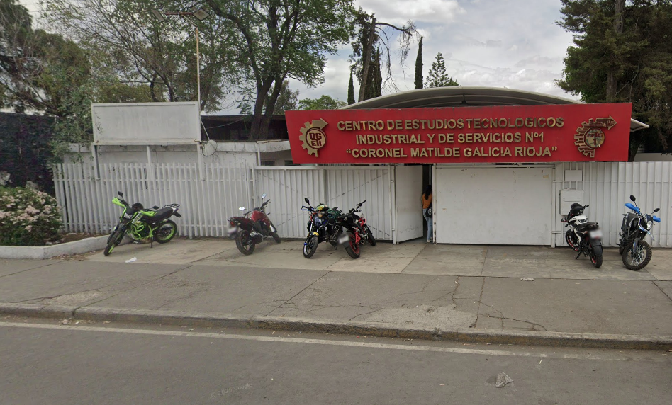 Fotografía en la que se muestra la entrada del plantel, conformada por rejas, muros y un portón blanco. Arriba del portón hay una placa de color rojo que en letras grandes y doradas dice CENTRO DE ESTUDIOS TECNOLÓGICOS INDUSTRIAL Y DE SERVICIOS NÚMERO 1. CORONEL MATILDE GALICIA RIOJA.